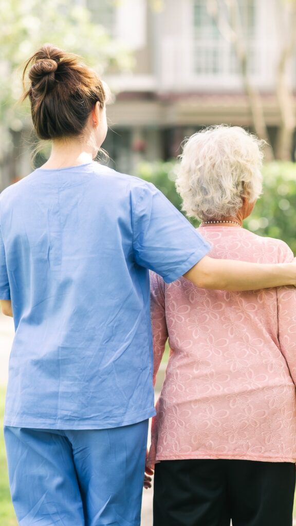 Pflegekraft, die eine ältere Frau beim Spaziergang im Freien begleitet